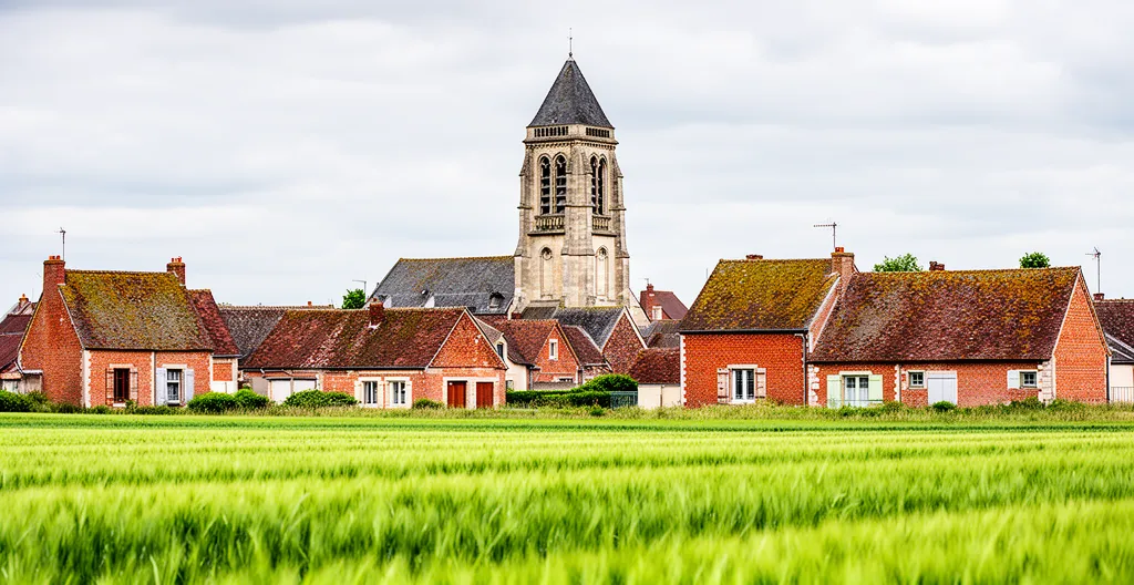 Village francilien avec clocher et champs verdoyants sous ciel voilé
